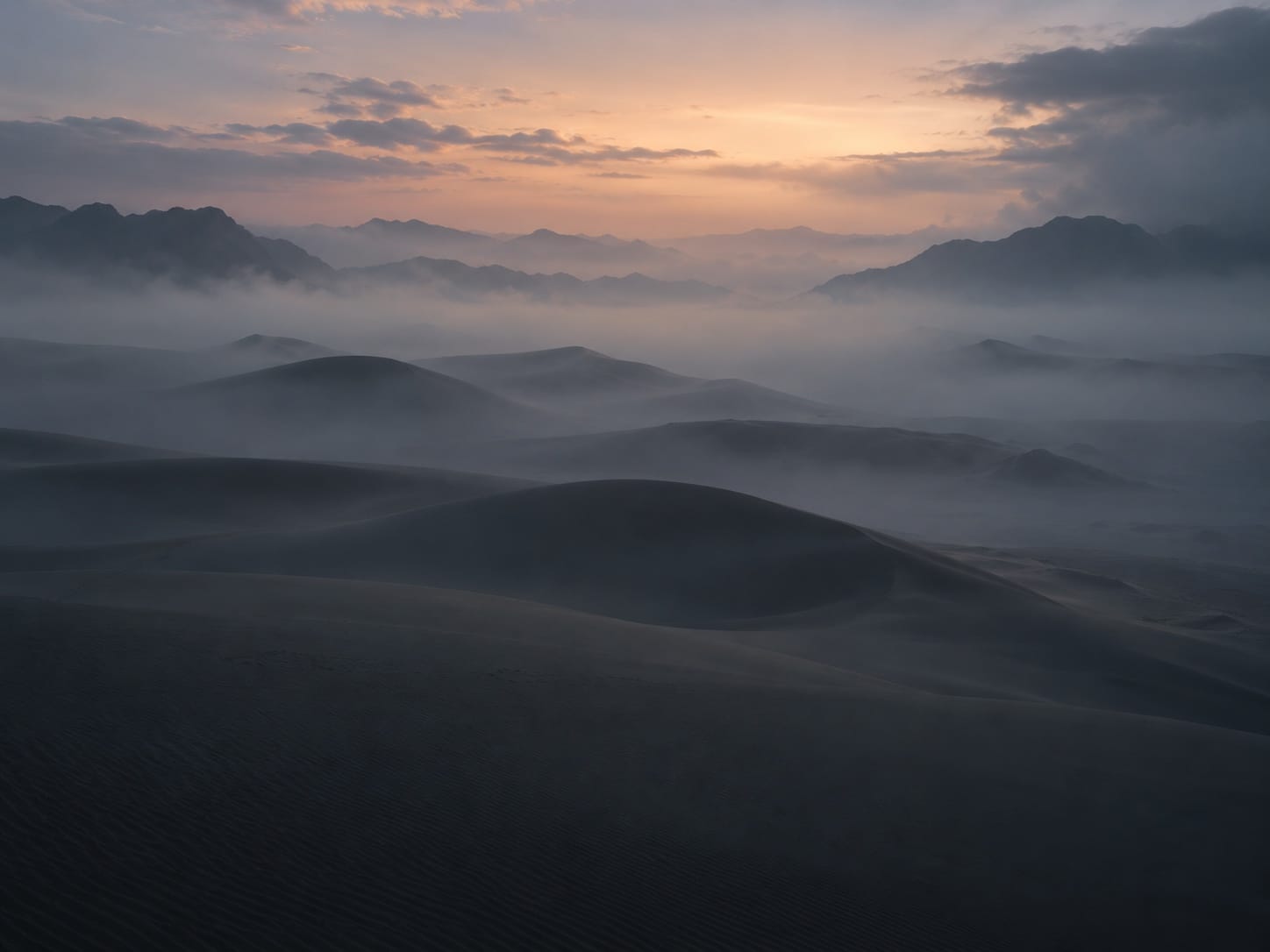 Desert dunes fading into dawn fog.